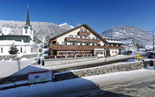 a large wooden building with a church in the snow at Hotel Sonne in Wildhaus