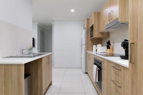 a kitchen with wooden cabinets and a white tile floor at Smart Suites Self Check-in Apartments - Freney Park in Brisbane