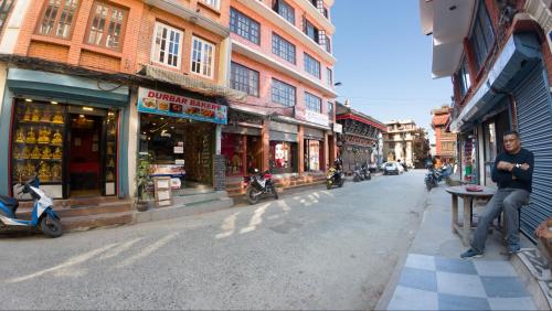 un hombre sentado en una mesa en una calle con edificios en Durbar Guest House, en Pātan