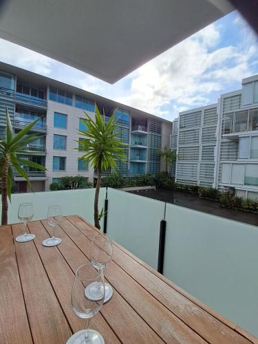 a wooden table with two wine glasses on a balcony at Pool-bikes-escooter! 2bed central in Auckland
