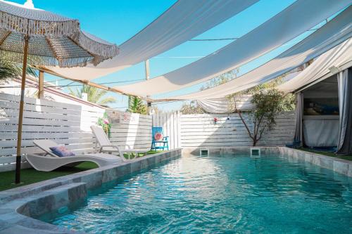 an outdoor pool with an umbrella and chairs and a swimming pool at וילה ריש - וילה מהממת למשפחות עם בריכה מחוממת וג'קוזי in Yarka
