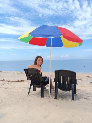 a woman sitting in a chair under an umbrella on the beach at Beach Clan Dorms in Alleppey