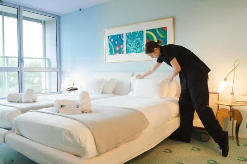 a woman is making a large bed in a hotel room at Hôtel Restaurant d'Occitanie in Toulouse