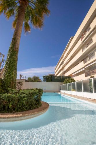- une piscine en face d'un bâtiment avec un palmier dans l'établissement Cap d'Antibes 2 bdr appartment with parking swimming pool and AC, à Antibes