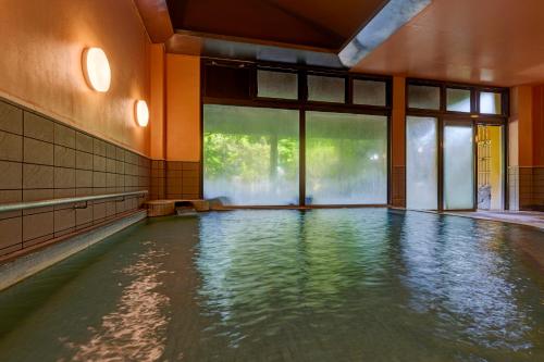 a swimming pool with water in a room with windows at Kamenoi Hotel Aso Park Resort in Aso