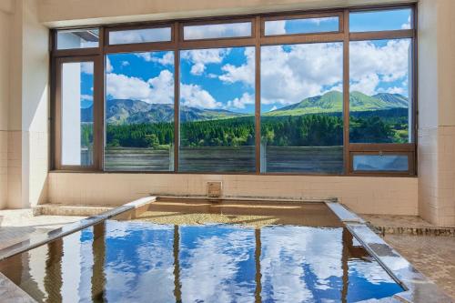 an empty swimming pool with a large window and mountains at Kamenoi Hotel Aso Park Resort in Aso