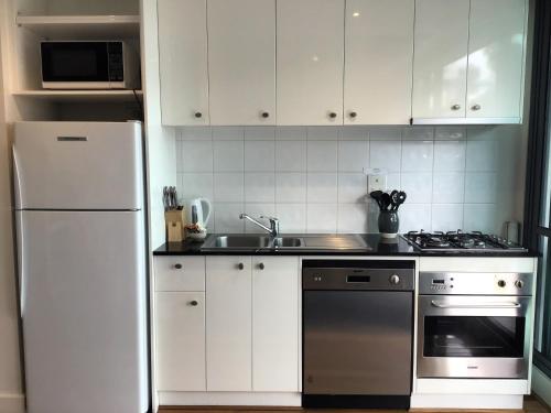 a kitchen with white cabinets and a white refrigerator at The Waterfront Apartments Geelong in Geelong
