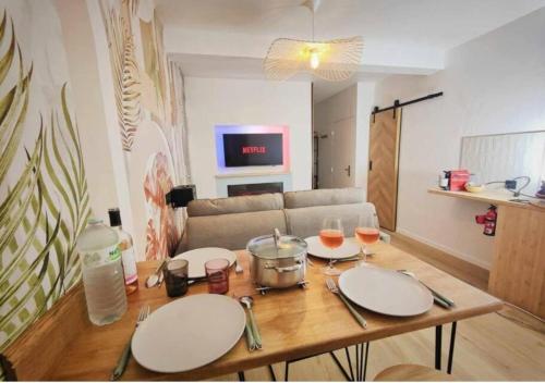 a table with plates and wine glasses and a couch at MRODBNB - Appart Neuf - Aperçu Mer - 25m Plage & Resto - Ciné - cheminée - Popcorn in Cancale