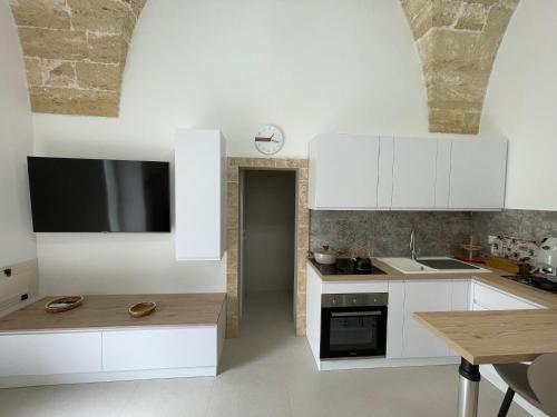a kitchen with white cabinets and a tv on the wall at Casina Carducci Apartment in Nardò