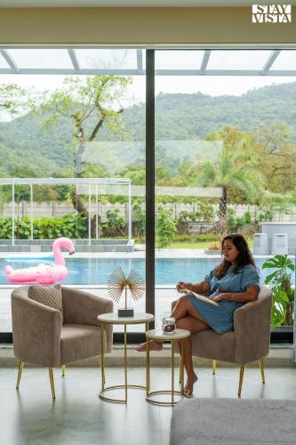 a woman sitting in a chair next to a pool at Middle Earth by Vieda - Part of StayVista with Pool in Karjat