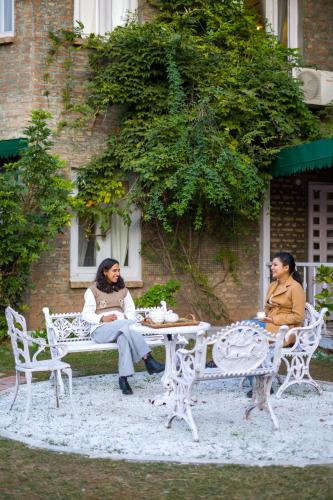 two women sitting on a bench in front of a building at Alaya Stays 3 BHK Pet-friendly with Garden - Chalet Vie Villa in Dharampur