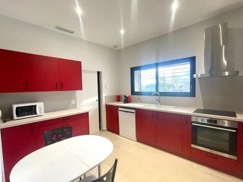 - une cuisine avec des placards rouges et une table dans l'établissement Maison d'exception climatisée mer et montagne, à Saint-Génis