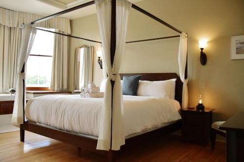 a bedroom with a canopy bed with white sheets at Tait House by Bower Boutique Hotels in Shediac