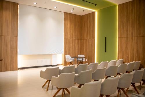 a conference room with white chairs and a projection screen at Cataratas Park Hotel e Eventos in Foz do Iguaçu