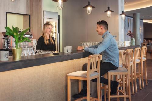 a man sitting at a bar talking to a woman at Holiday Inn - the niu, Yen Hamburg City by IHG in Hamburg