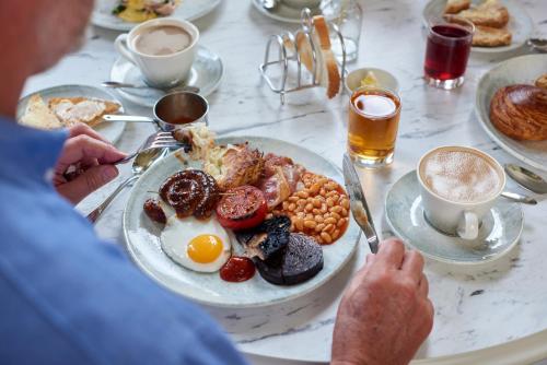 een man aan een tafel met een bord ontbijtproducten bij Reserve, by Warner Hotels - Heythrop Park in Chipping Norton