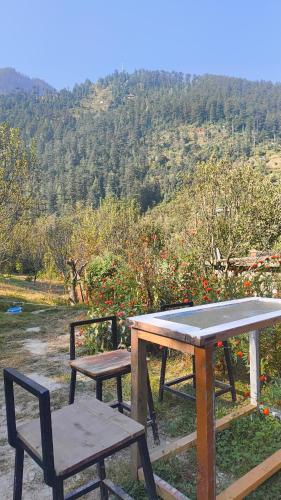 a picnic table and two chairs with a view of a mountain at Seasons By Hostalgic in Jibhi