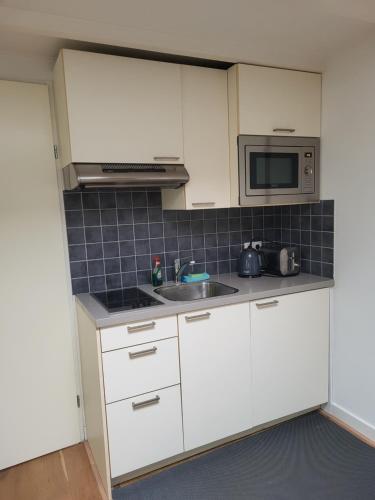 a kitchen with white cabinets and a sink and a microwave at Spacious private guest house in Hilversum