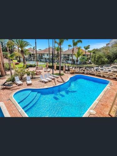a large blue swimming pool with chairs and palm trees at Loft Villa Pool Spa & Beach Sleeps Six! in Mandurah