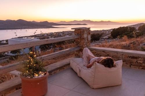 a woman laying in a chair on a balcony with the sunset at Deja Blue Villa 1 in Agios Georgios
