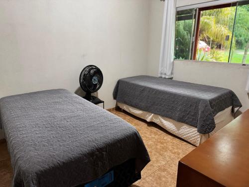 a room with two beds and a fan and a window at Sítio Matinha - Chap dos Veadeiros - São João dAliança in São João da Aliança