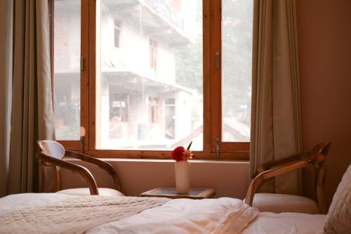 a bedroom with a bed and two chairs and a window at Zankhrpas A Himalayan Home - Manali in Manāli