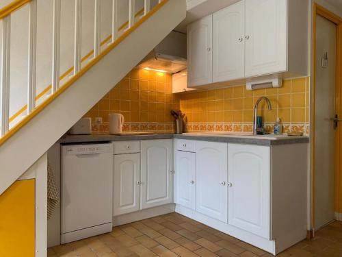 une cuisine avec des placards blancs et un escalier dans l'établissement Charmante maison proche plage, à Saint-Cyprien