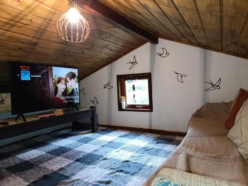 a living room with a tv and a bed at Casa Cipreste no Refúgio Pinheiro Beira Rio in Sapucaí-Mirim