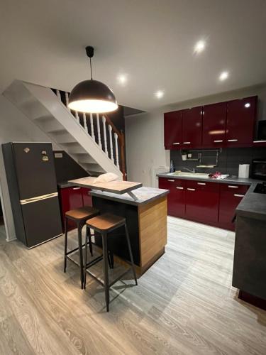 une cuisine avec des placards rouges et un îlot de cuisine avec des tabourets dans l'établissement l'HIRONDELLE, à Les Goths