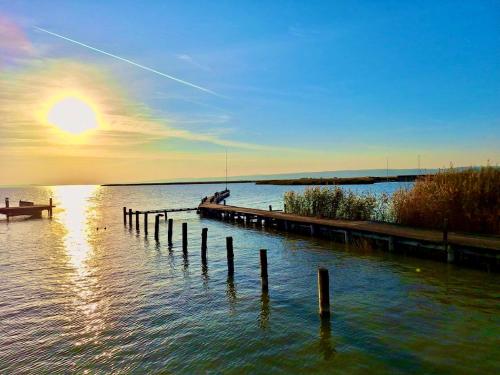 a dock in the water with the sun setting at Apartments C'EST LA SEA - Whirlpool-Suite oder Dachterrassen-Suite in Neusiedl am See