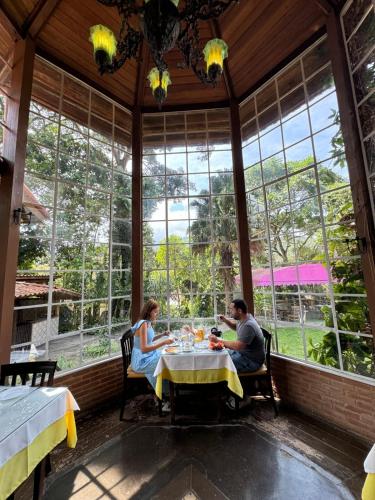 a man and woman sitting at a table in a room with windows at Pousada Olho D'Água in Visconde De Maua