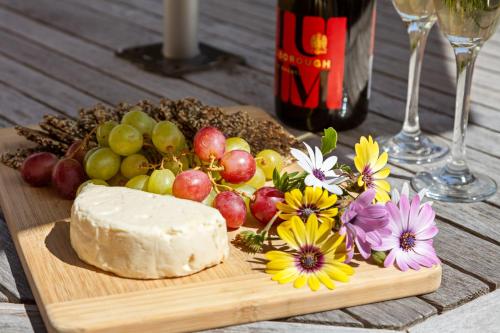 a wooden cutting board with cheese and grapes and flowers at Ocean Beach Wainui in Gisborne