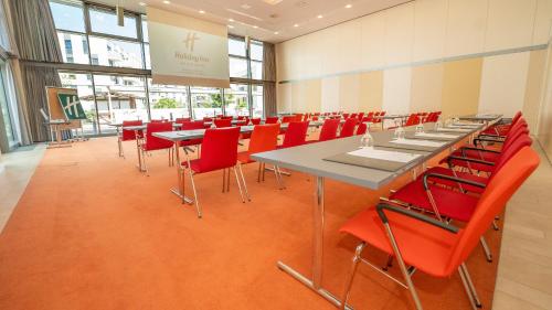a conference room with tables and red chairs at Holiday Inn Berlin Airport - Conference Centre by IHG in Schönefeld