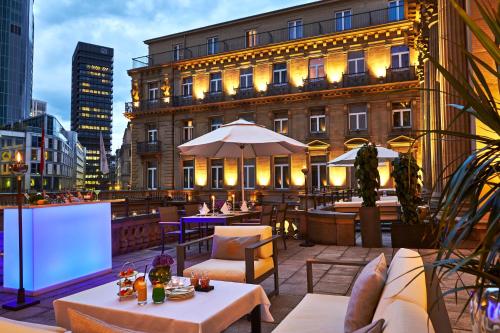 a rooftop patio with tables and chairs and a building at Steigenberger Icon Frankfurter Hof in Frankfurt/Main