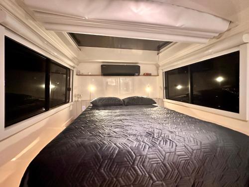 a bed in the back of a rv with two windows at Refúgio estelar com vista para represa in Joanópolis