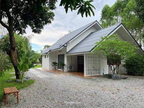 a white house with a tree and a bench at Phiratara River House บ้าน พิรธารา ริมแม่น้ำปราจีนบุรี in Ban Suan Phlu