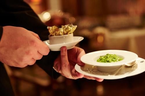 a person holding two bowls of food on a plate at Steigenberger Icon Frankfurter Hof in Frankfurt/Main