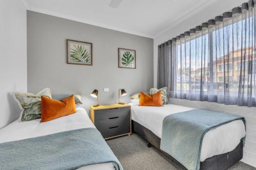 two beds in a room with a window at The Palms Apartments in Merimbula