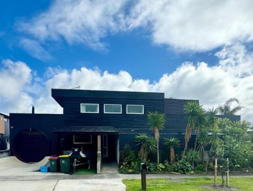 a black house with palm trees in front of it at Electric Waihi Beach House - family & dog friendly, close to beach, pool table, outdoor fire room, skate ramp in Bowentown