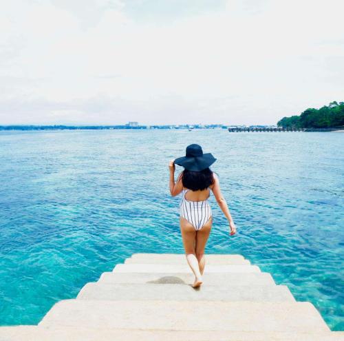 a woman in a hat walking on a dock in the water at Crusoe Cabins Costa Azalea in Davao City