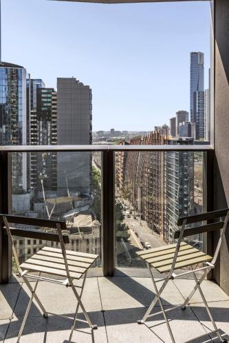 two chairs on a balcony with a view of a city at Orange Stay at Melbourne Quarter in Melbourne