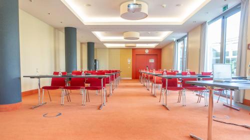 a conference room with tables and red chairs at Holiday Inn Berlin Airport - Conference Centre by IHG in Schönefeld