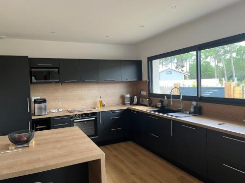 une cuisine avec des armoires noires et une grande fenêtre dans l'établissement Montalivet maison neuve 1Km Plage, à Montalivet-les-Bains