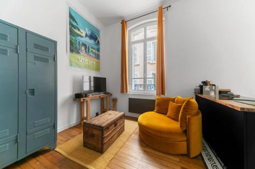 un salon avec une chaise jaune et une table dans l'établissement Le Plaisance - Appartement de Standing proche Opéra et Parcs, à Vichy