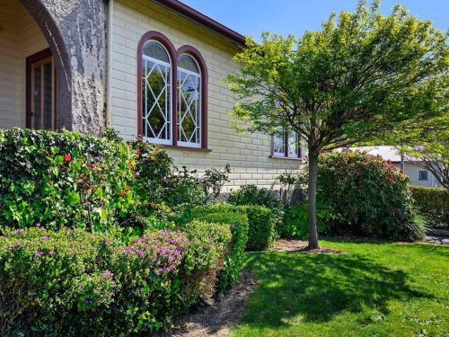 a house with a tree and flowers in the yard at Santos 20th century cottage in South Burnie