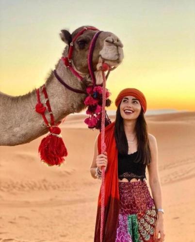 a woman standing next to a camel in the desert at Merzouga Sara Luxury Camp in Merzouga
