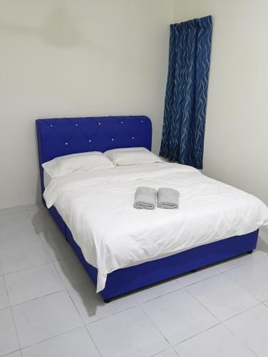 a blue bed with two slippers on top of it at The Welcome Mat Homestay in Seri Iskandar