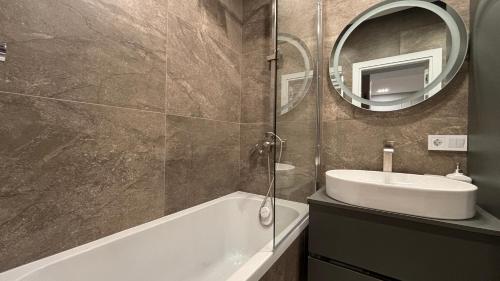 un bagno con un lavandino, una vasca e uno specchio di Nova ApartHotel a Chişinău