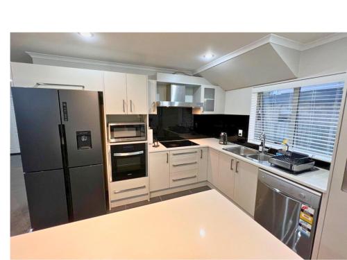 a kitchen with white cabinets and a black refrigerator at Bright&Cozy Room with attached private bathroom - On street parking only in Auckland