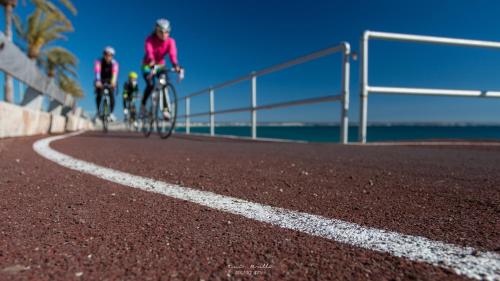 two people riding bikes on a road near the ocean at Hotel Amic Can Pastilla in Can Pastilla
